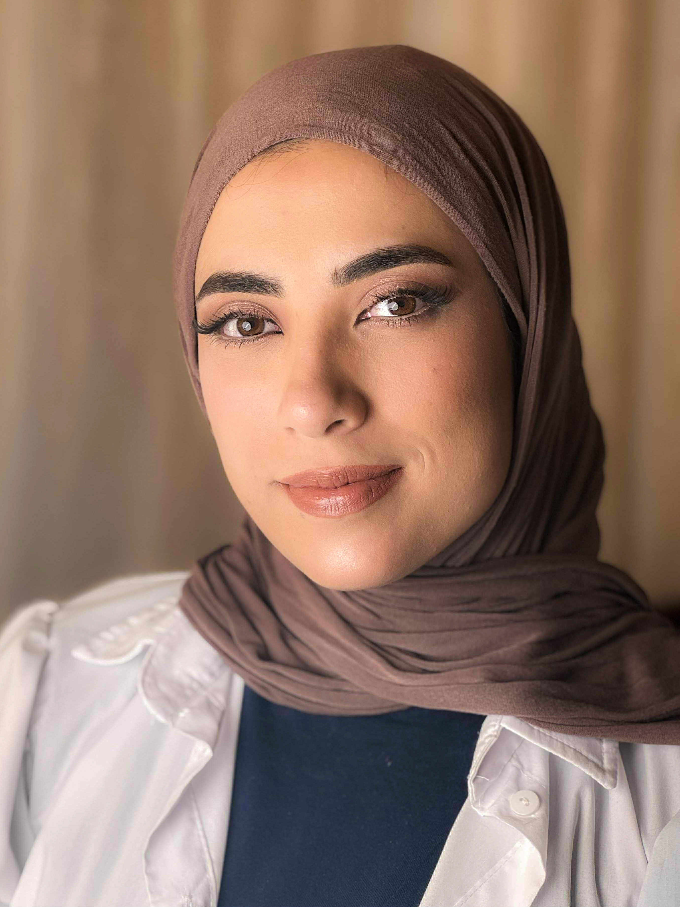 Natural glowing makeup with defined brows and nude-pink lips in brown hijab